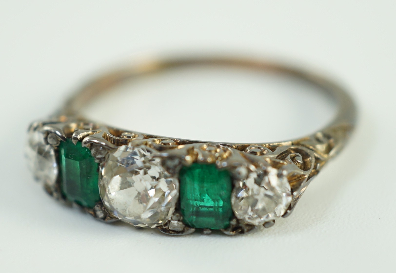 An early 20th century 18ct gold, three stone diamond and two stone emerald set half hoop ring